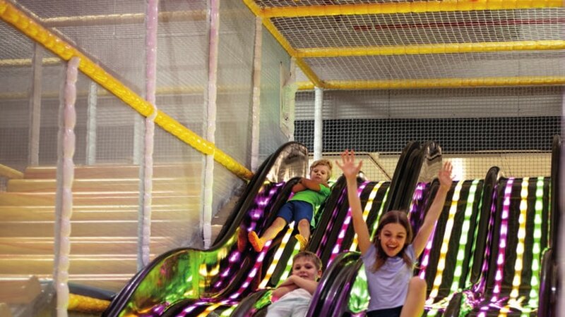 Drei Kinder rutschen auf den bunt beleuchteten Wellenrutschen ins B&auml;llebad